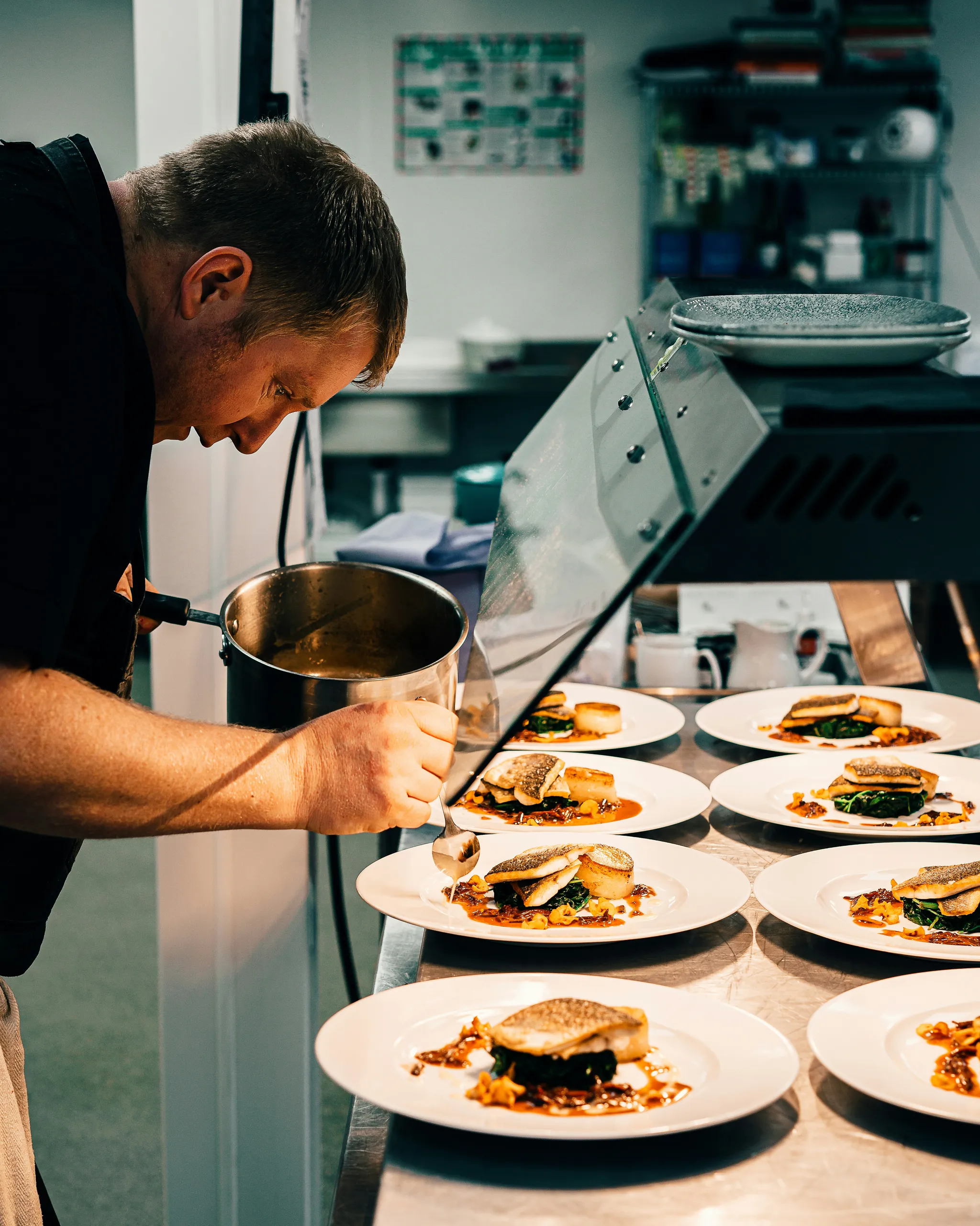 El cocinero napa la salsa sobre elegantes platos servidos en vajilla blanca