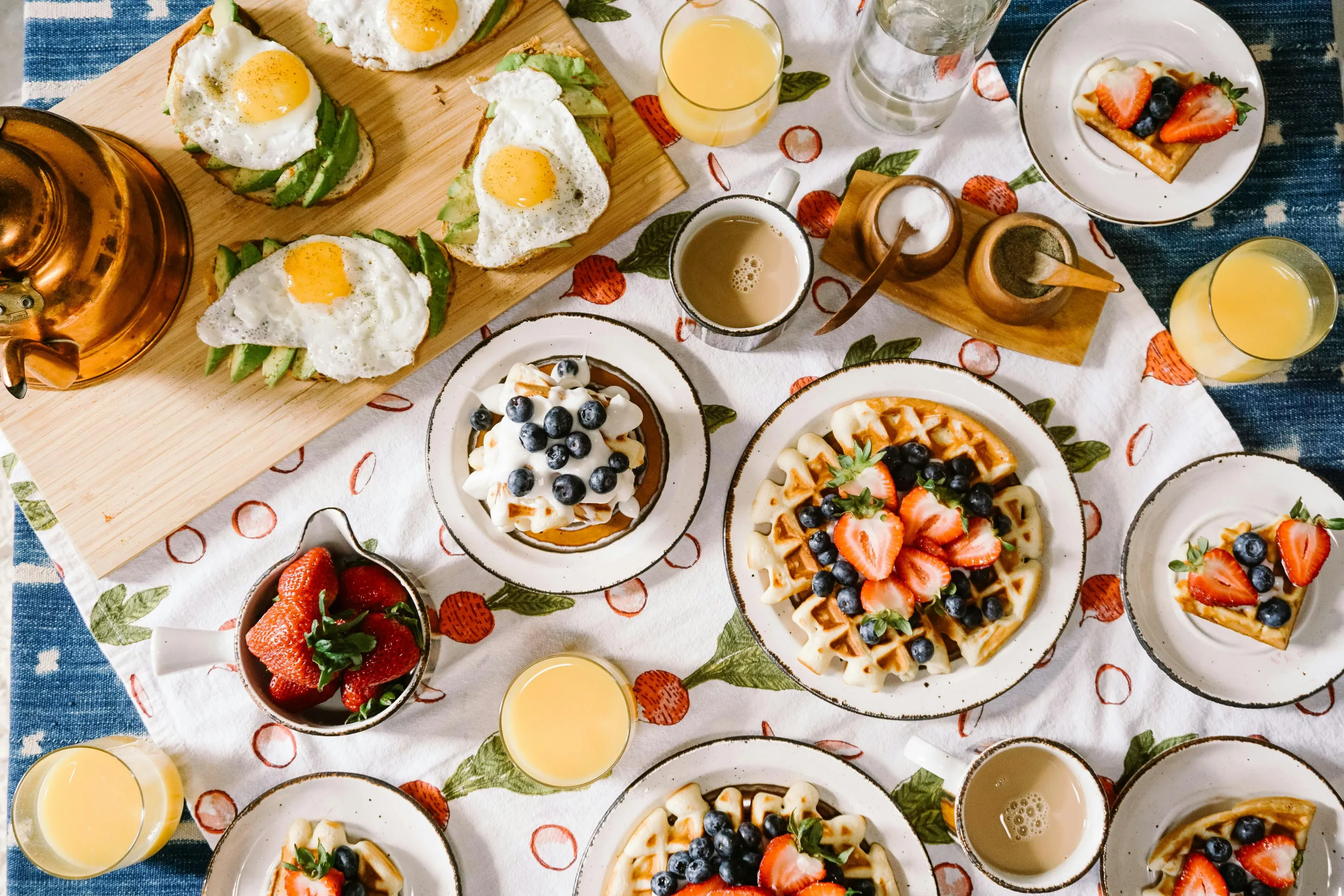 Mesa de desayuno llena de huevos, gofres, fruta fresca y zumo de naranja